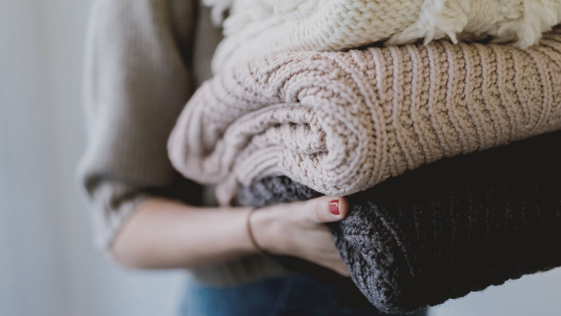 Close-up of woman carrying knitted sweaters. [Image: Dan Gold at Unsplash]